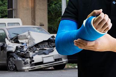 Person with arm in blue cast standing near a damaged car—debunking car accident claim myths in Georgia.