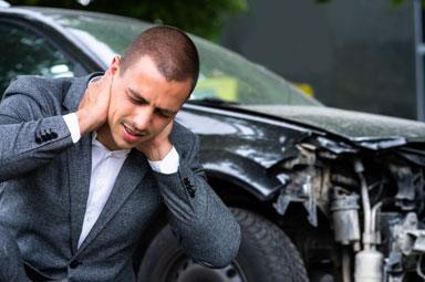Man holding neck beside damaged car, symbolizing pain and suffering claims in Georgia.