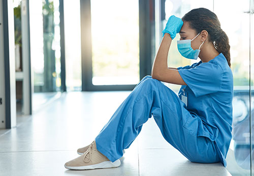 Stressed medical professional in scrubs sitting on the floor of a corridor.