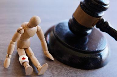 Wooden figure with injured knee beside a gavel, symbolizing personal injury legal claims.
