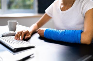 Injured person with arm cast typing on a keyboard, highlighting damages in Georgia injury lawsuits.